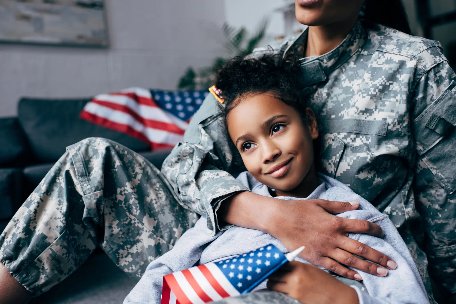 A U.S. servicewoman seated with her young daughter in front of an American flag, representing the service-disabled veterans this certification is built around