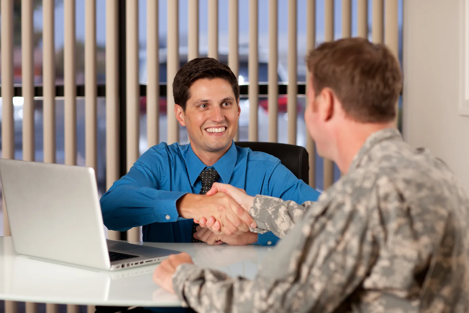 A uniformed U.S. servicemember shaking hands with a businessman across a desk, representing the veteran-owned business relationship Norvet MSP brings to federal and prime contracting