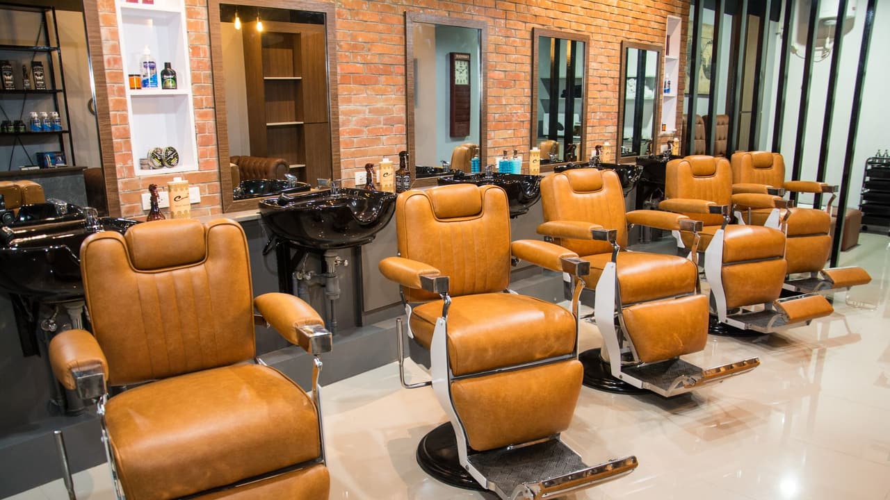 Stock photo: a barber shop with tan leather reclining chairs in a row on a polished floor, with a brick wall and mirrors behind and nobody in it.