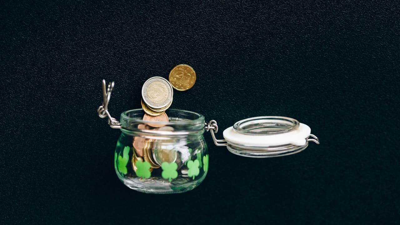 Stock photo: coins falling into a glass jar against a dark background.