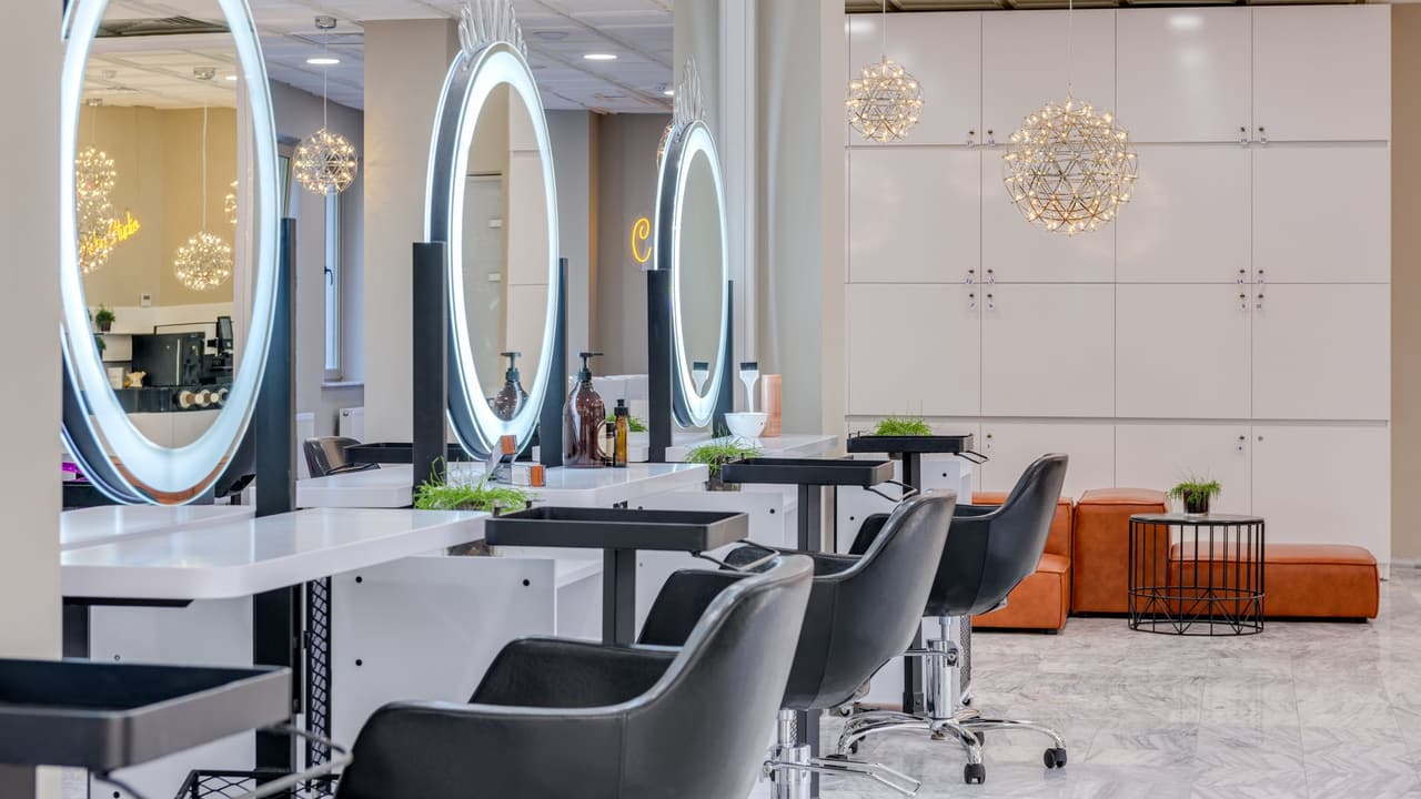 Stock photo: a bright hair salon with round lighted mirrors and styling chairs, with nobody in it.