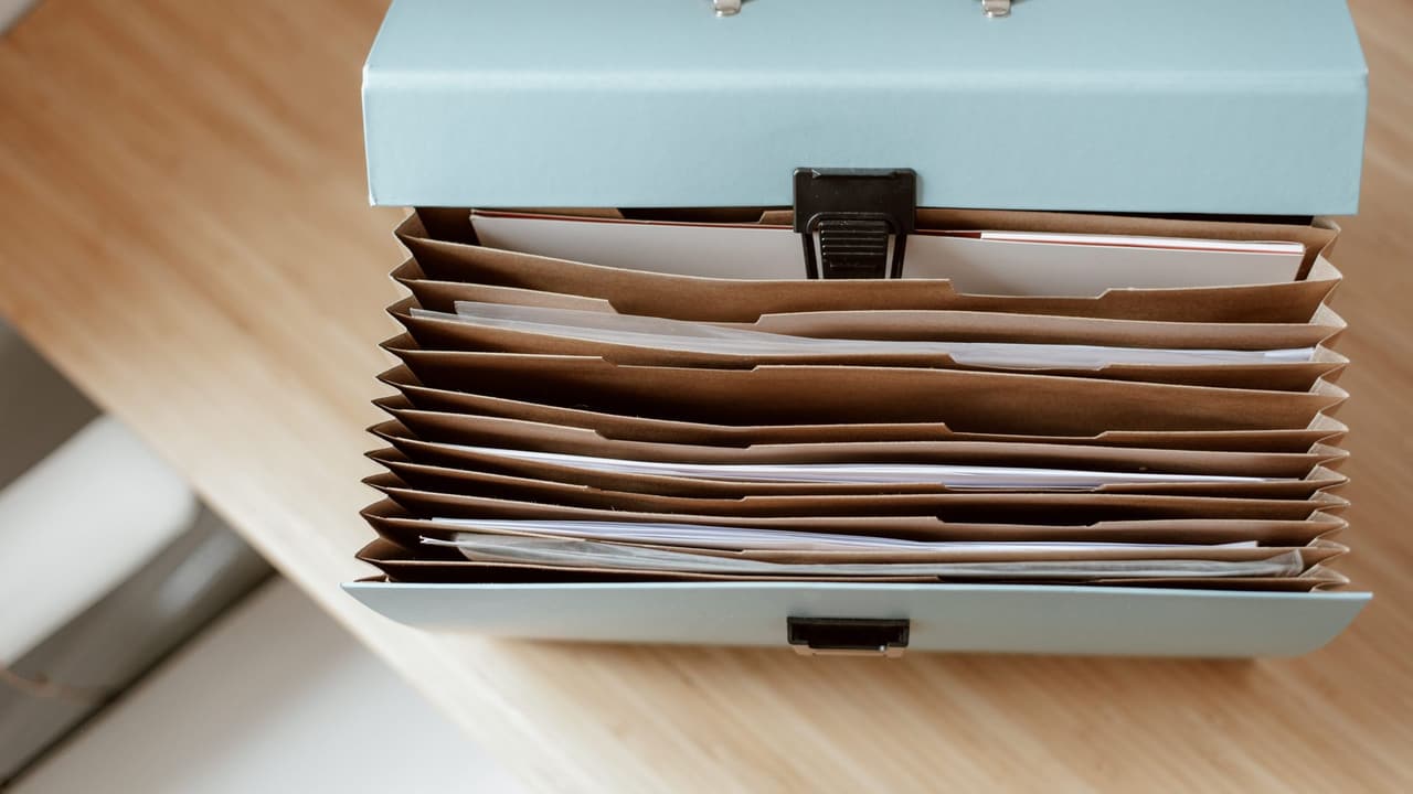 Stock photo: an accordion file organizer holding brown paper folders, seen from above on a wooden desk.