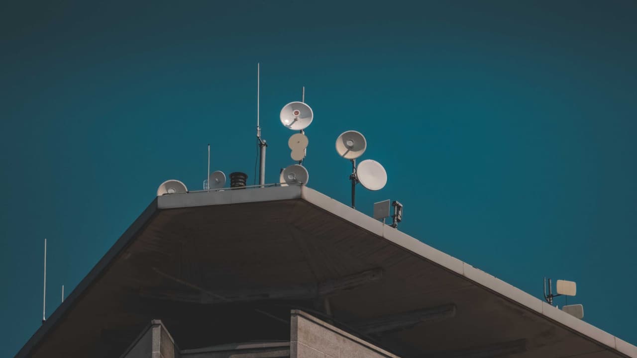 Stock photo: a satellite dish and antennas on a rooftop against a blue sky.
