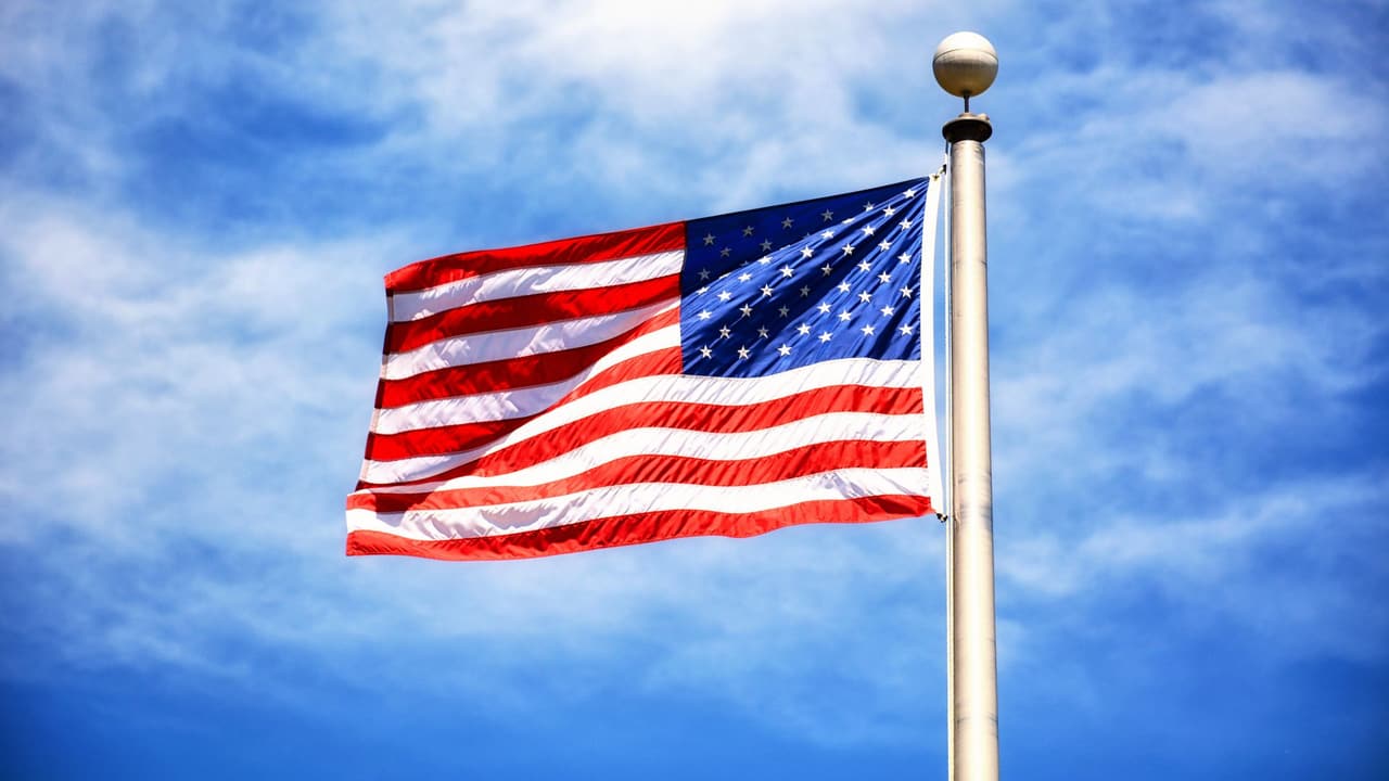 Stock photo: an American flag flying on a pole against a cloudy sky.